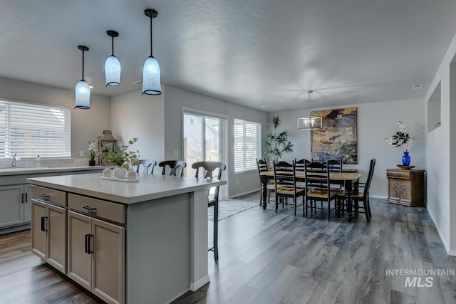 kitchen with light countertops, wood finished floors, a center island, gray cabinets, and a kitchen breakfast bar