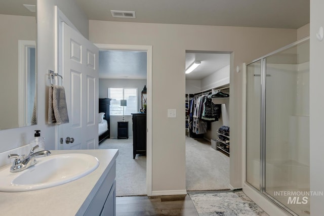 bathroom featuring a stall shower, vanity, wood finished floors, a spacious closet, and visible vents