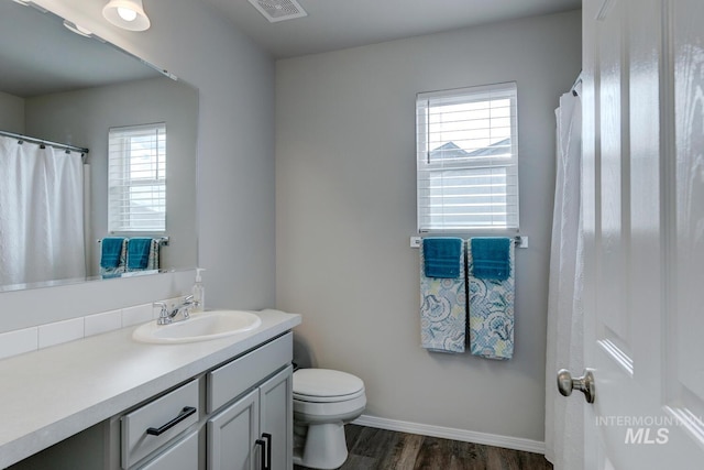 bathroom with toilet, vanity, wood finished floors, baseboards, and visible vents