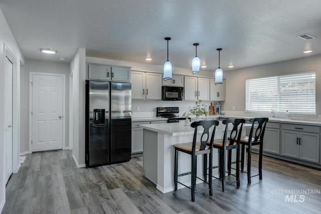 kitchen featuring a kitchen breakfast bar, refrigerator with ice dispenser, stainless steel range with electric cooktop, visible vents, and black microwave