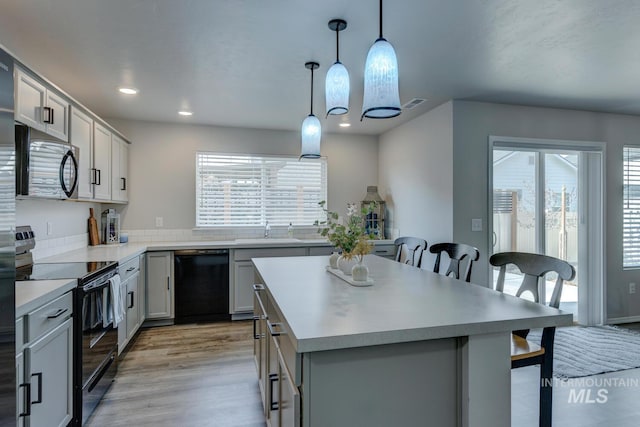 kitchen featuring light wood finished floors, a kitchen island, a sink, black appliances, and a kitchen breakfast bar