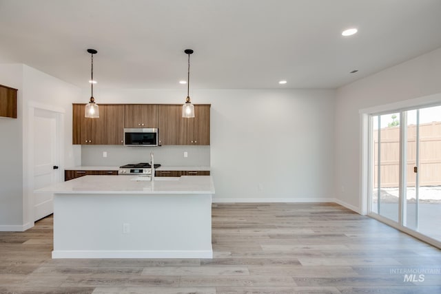 kitchen featuring pendant lighting, backsplash, a kitchen island with sink, light wood-type flooring, and stainless steel appliances