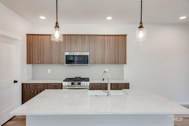 kitchen with light stone countertops, hanging light fixtures, appliances with stainless steel finishes, and tasteful backsplash