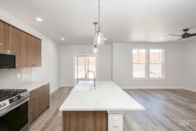 kitchen with decorative backsplash, appliances with stainless steel finishes, sink, and an island with sink