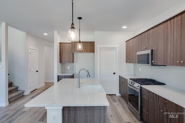 kitchen with sink, decorative light fixtures, decorative backsplash, a center island with sink, and appliances with stainless steel finishes