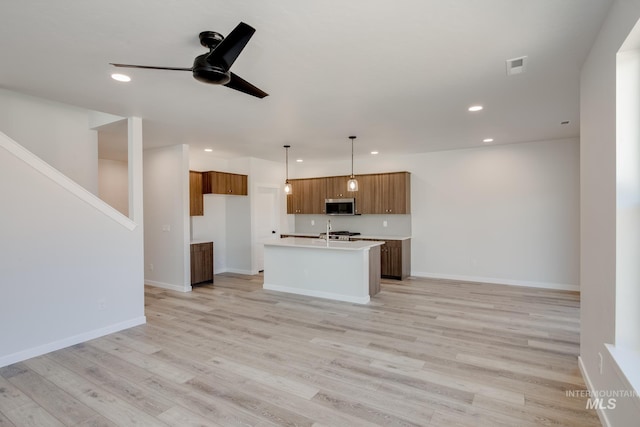 kitchen featuring ceiling fan, a center island with sink, pendant lighting, and light hardwood / wood-style floors