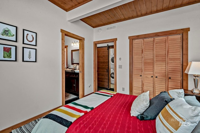 bedroom featuring ensuite bathroom, beamed ceiling, wood ceiling, and stacked washer / drying machine