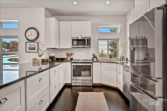 kitchen with decorative backsplash, appliances with stainless steel finishes, dark wood-type flooring, dark stone countertops, and white cabinetry