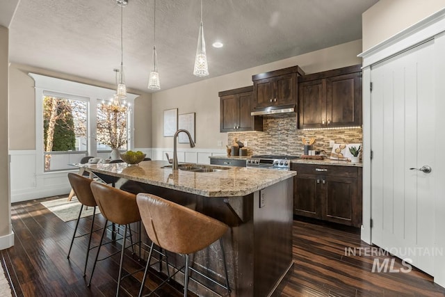 kitchen featuring light stone countertops, dark hardwood / wood-style flooring, sink, an island with sink, and stainless steel range with gas stovetop