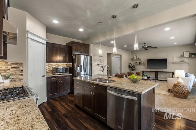 kitchen with stainless steel appliances, light stone counters, dark wood-type flooring, and an island with sink