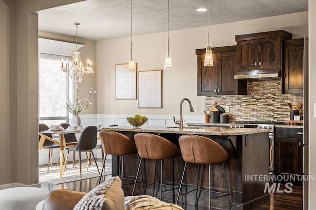 kitchen featuring dark wood-type flooring, sink, an island with sink, light stone counters, and dark brown cabinetry