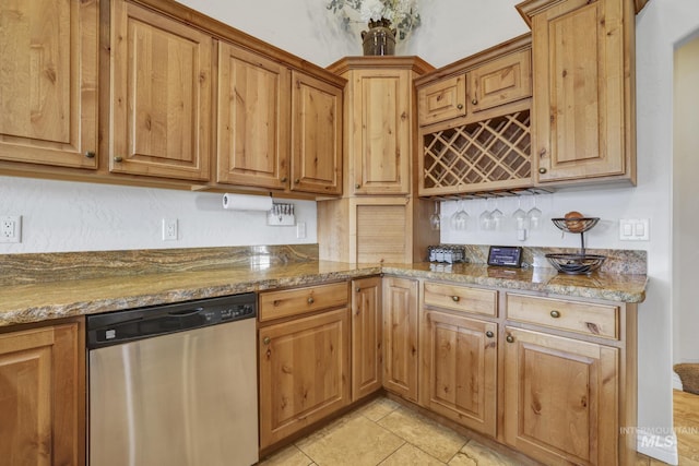 kitchen with light tile patterned flooring, dark stone countertops, and stainless steel dishwasher