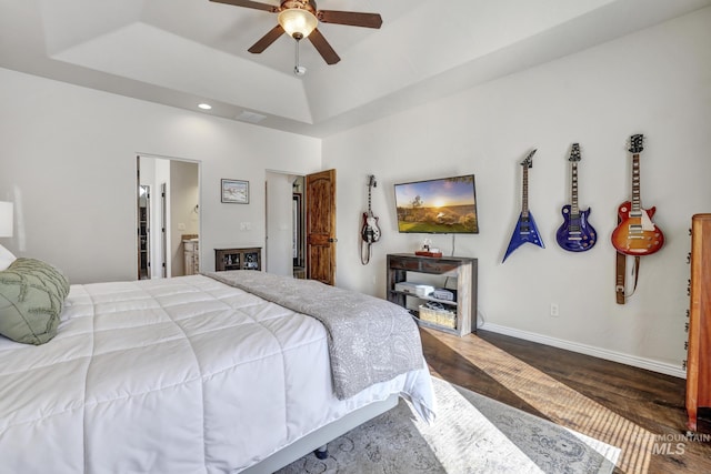 bedroom featuring visible vents, a raised ceiling, ensuite bathroom, wood finished floors, and baseboards