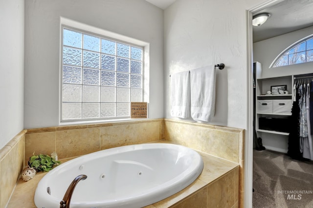 bathroom featuring a spacious closet and a tub with jets