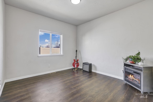 spare room with a glass covered fireplace, visible vents, baseboards, and wood finished floors