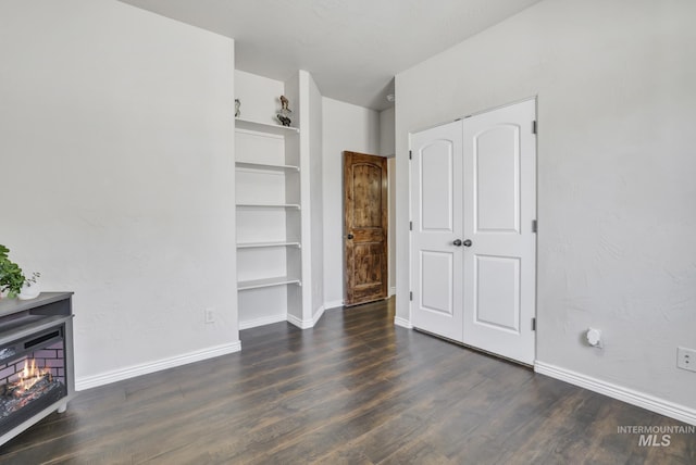 unfurnished bedroom featuring a closet, a warm lit fireplace, baseboards, and wood finished floors