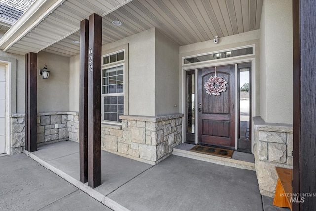 property entrance with stone siding, stucco siding, and covered porch