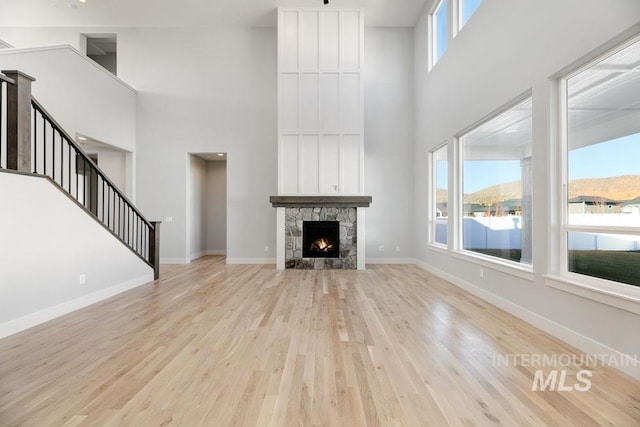 unfurnished living room featuring a high ceiling, baseboards, stairs, and light wood-style floors