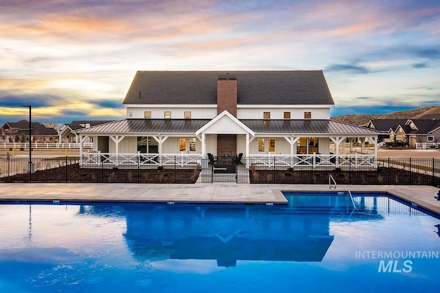 pool at dusk with a community pool, covered porch, and fence private yard