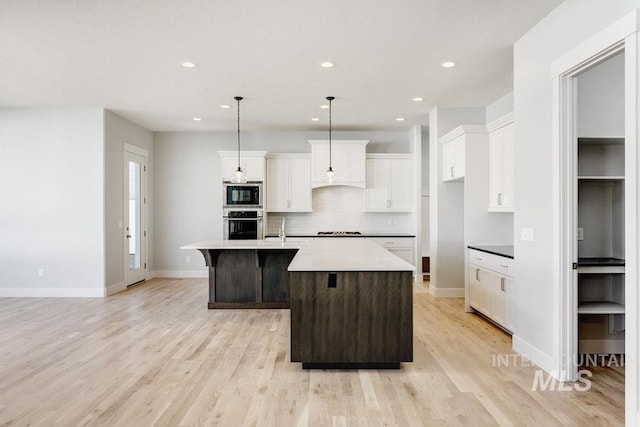 kitchen with decorative backsplash, light wood-style floors, built in microwave, a kitchen island with sink, and stainless steel oven