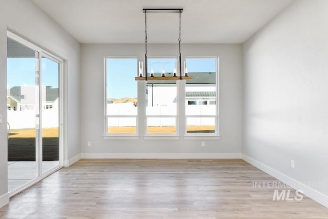 unfurnished dining area featuring a chandelier, a healthy amount of sunlight, and light wood finished floors