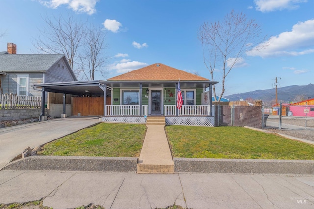 bungalow-style home featuring driveway, a porch, an attached carport, fence, and a front lawn