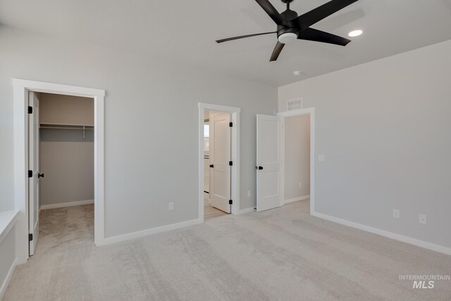 unfurnished bedroom with a walk in closet, ceiling fan, a closet, and light colored carpet