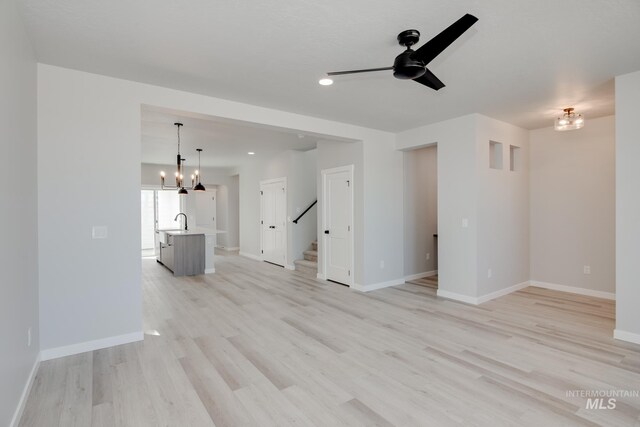 unfurnished living room with ceiling fan with notable chandelier, light hardwood / wood-style flooring, and sink