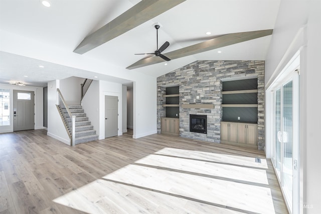 unfurnished living room featuring a stone fireplace, ceiling fan, light hardwood / wood-style flooring, and vaulted ceiling with beams