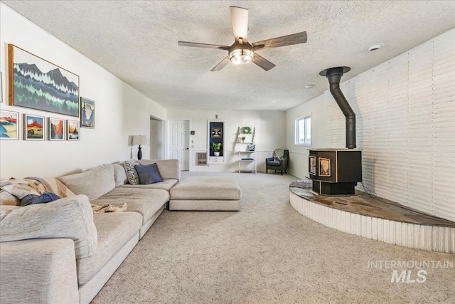 living room featuring carpet, a textured ceiling, a wood stove, and ceiling fan