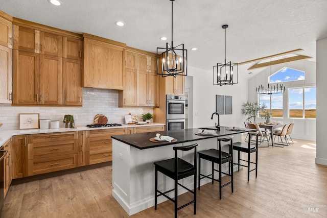 kitchen with a center island with sink, lofted ceiling with beams, light hardwood / wood-style floors, and appliances with stainless steel finishes