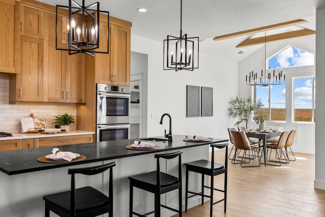 kitchen with sink, tasteful backsplash, light hardwood / wood-style flooring, double oven, and lofted ceiling