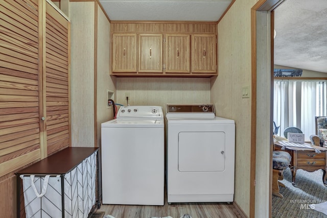 clothes washing area with cabinets, independent washer and dryer, a textured ceiling, and light wood-type flooring