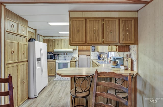 kitchen with sink, a kitchen breakfast bar, independent washer and dryer, kitchen peninsula, and white appliances