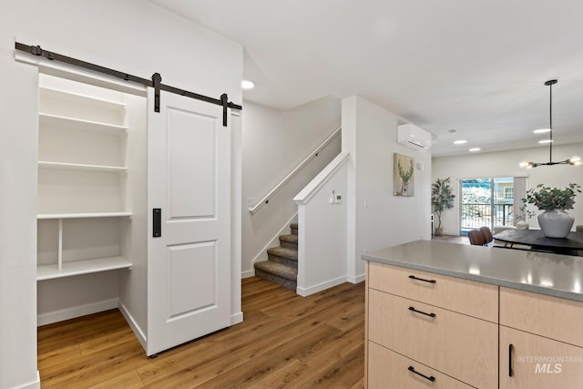 kitchen with a wall mounted air conditioner, a barn door, light wood-style flooring, and light brown cabinetry