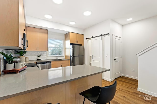 kitchen with a sink, a barn door, a kitchen bar, a peninsula, and stainless steel appliances