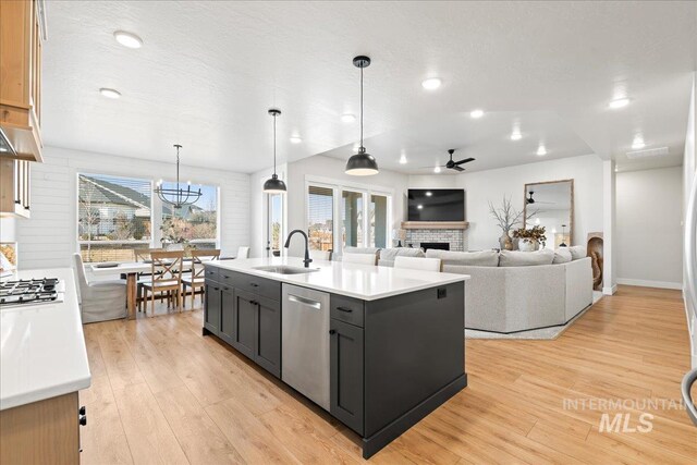 kitchen featuring a fireplace, stainless steel appliances, light countertops, light wood-style floors, and a sink