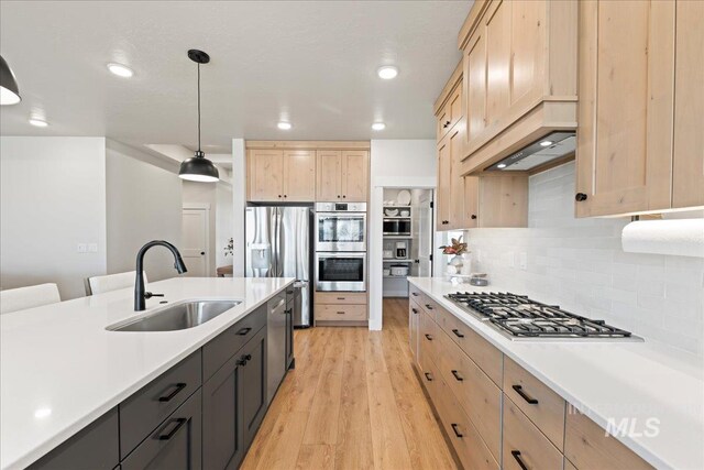 kitchen featuring light brown cabinetry, appliances with stainless steel finishes, light wood-type flooring, and a sink