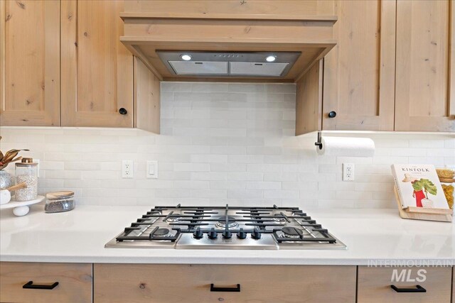 kitchen featuring custom exhaust hood, light countertops, light brown cabinetry, stainless steel gas cooktop, and backsplash