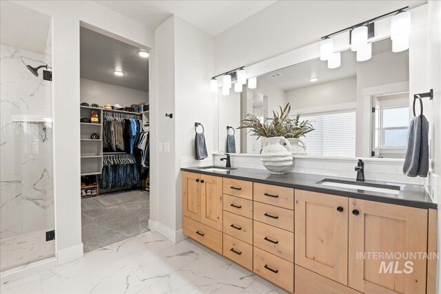 bathroom featuring a walk in closet, marble finish floor, a marble finish shower, double vanity, and a sink