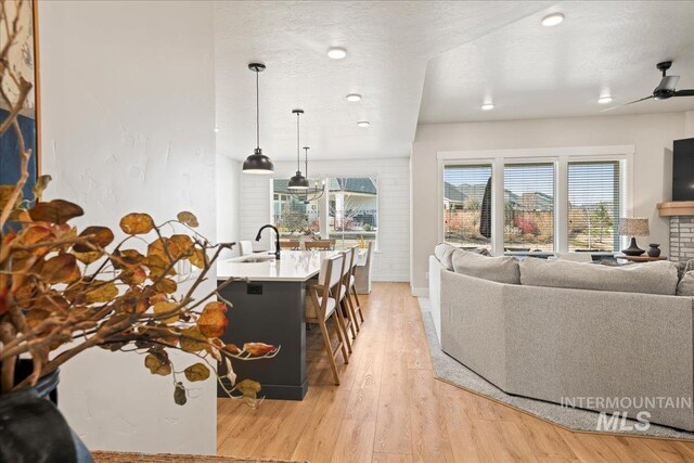 living area with light wood-type flooring, ceiling fan, and a textured ceiling