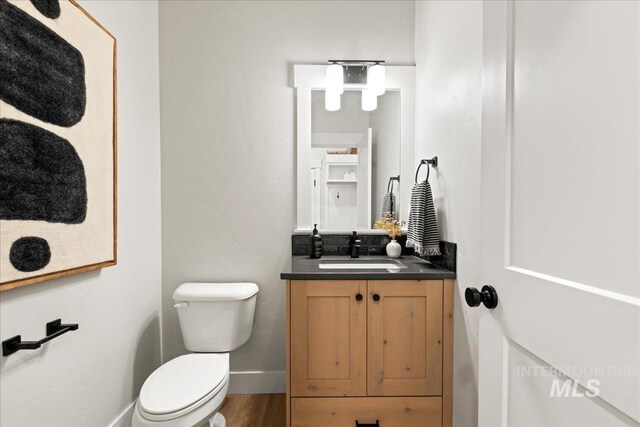 bathroom featuring toilet, baseboards, wood finished floors, and vanity