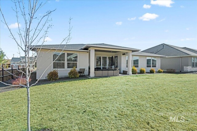 rear view of property featuring an outdoor hangout area, a yard, fence, and stucco siding