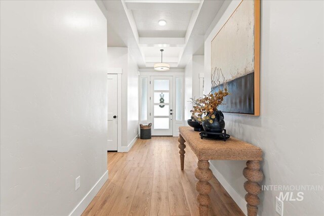 doorway with a tray ceiling, light wood finished floors, and baseboards