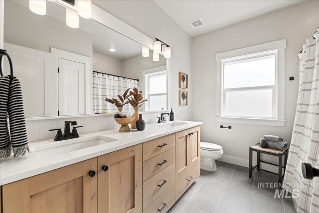 bathroom with double vanity, visible vents, toilet, and a sink