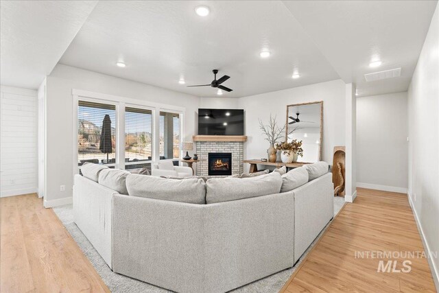 living area with light wood-type flooring, visible vents, a fireplace, and ceiling fan