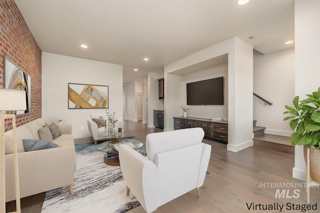 living room featuring a textured ceiling, wood finished floors, recessed lighting, stairway, and brick wall