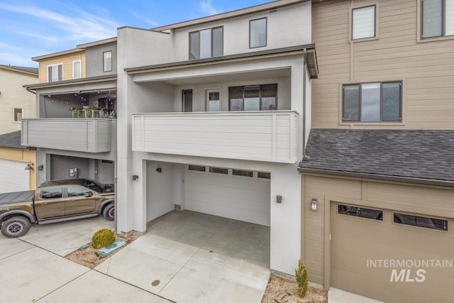 multi unit property featuring concrete driveway, stucco siding, a garage, and a shingled roof