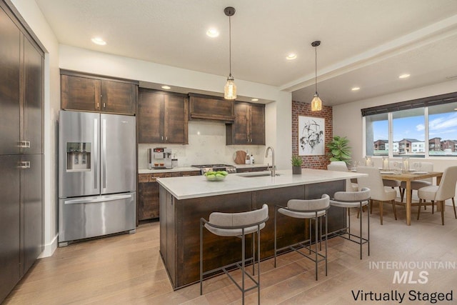 kitchen with dark brown cabinets, light countertops, stainless steel refrigerator with ice dispenser, and a sink