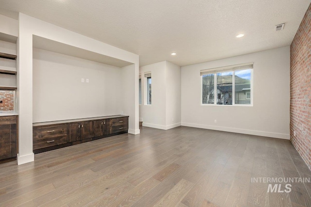 unfurnished room featuring wood finished floors, baseboards, brick wall, and a textured ceiling